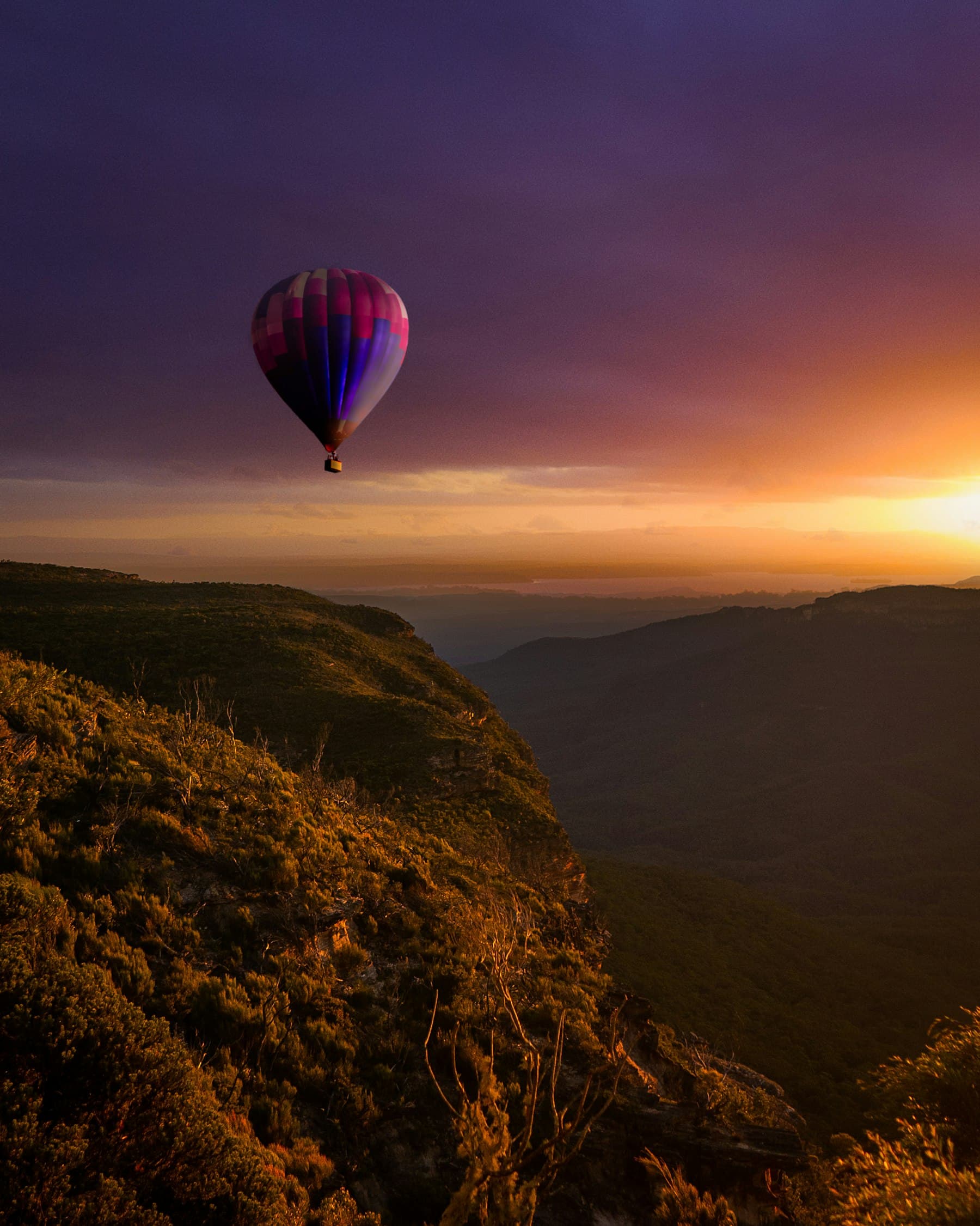 A hot-air balloon rising over mountains at sunrise